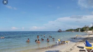 A beach with clear water, people swimming, and a few beach chairs. - Executive Inn (Pensacola)