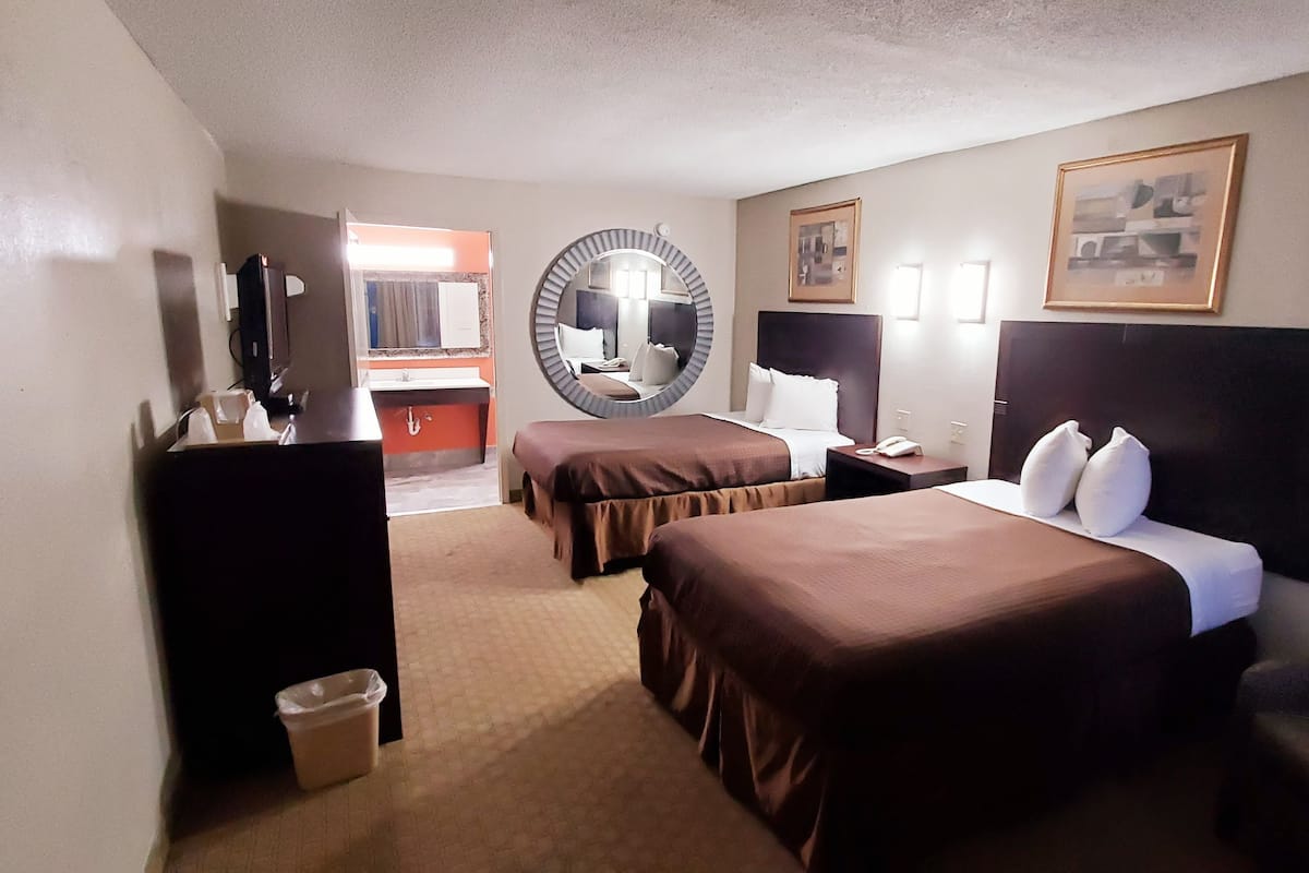 A hotel room with two beds, a desk, a chair, a mirror, and a bathroom visible through an open door.