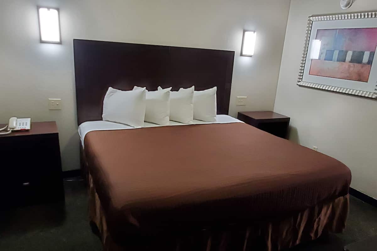 A hotel room with a large bed, two bedside tables, a nightstand, and a wall-mounted light fixture.