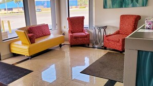 A lobby with a yellow sofa, red armchairs, a small round table, and a view of the outside. - Executive Inn (Pensacola)