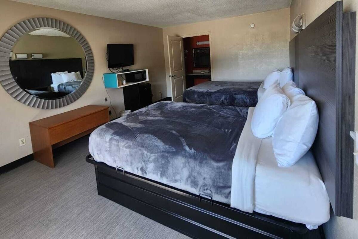 A hotel room with a large bed, a round mirror, a TV, a desk, and a wardrobe.