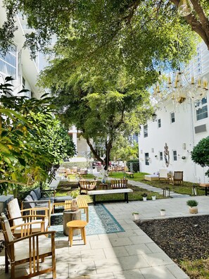 An outdoor seating area with wooden furniture, a blue patterned rug, and a tree providing shade. - Aqua Hotel (Fort Lauderdale)