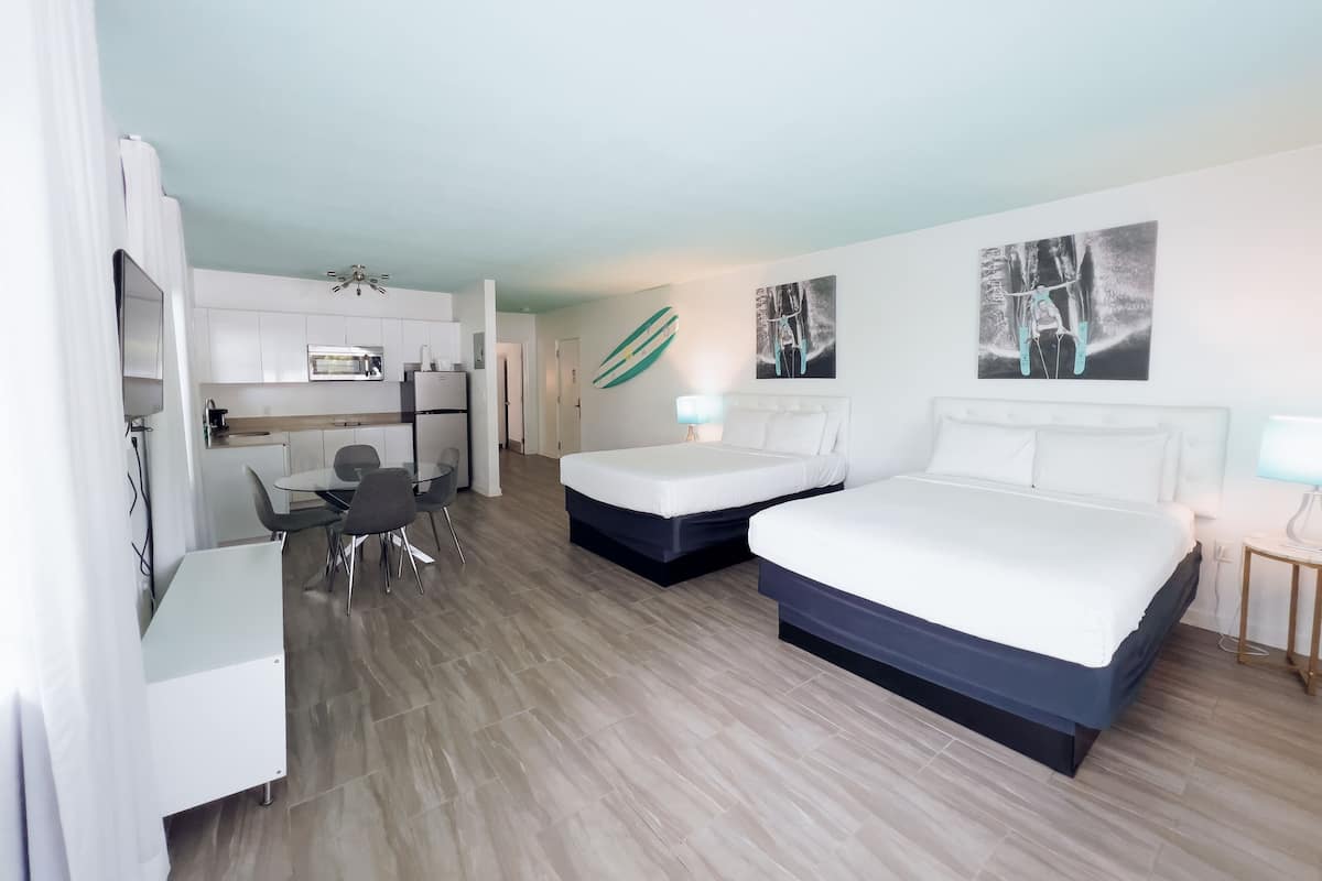 Une chambre d’hôtel avec deux lits, une kitchenette, un coin repas et des œuvres d’art aux murs.