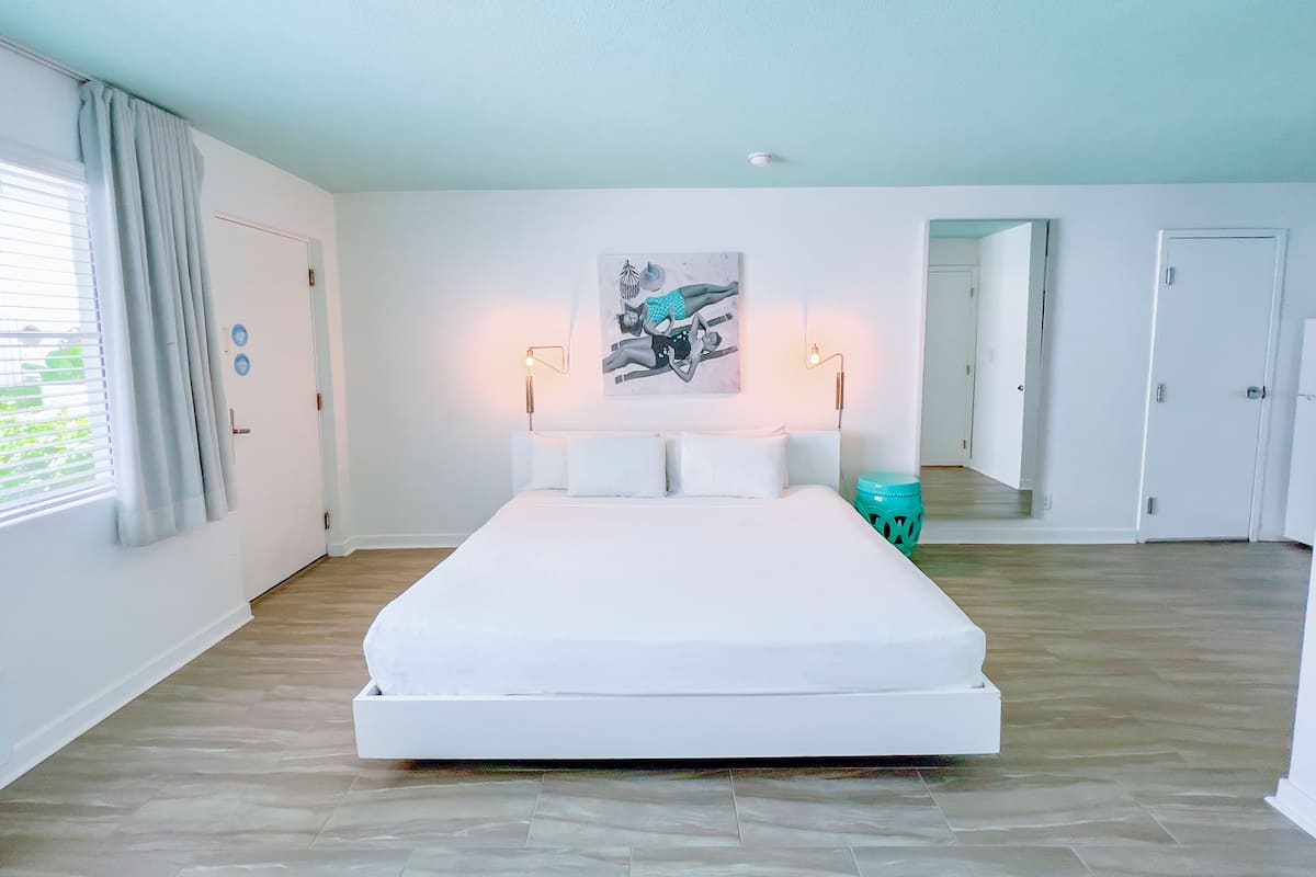 Une chambre spacieuse avec un grand lit, deux lampes de chevet, une œuvre d’art accrochée au mur et une fenêtre avec des rideaux.