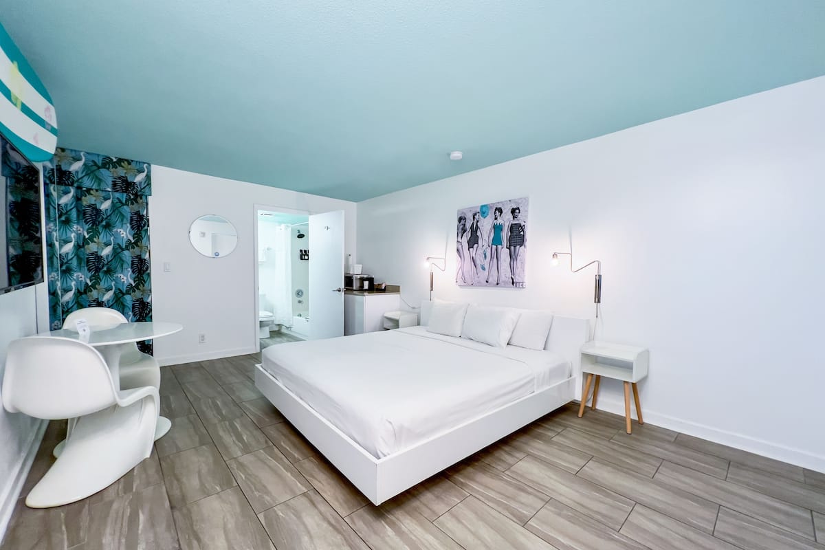 Une chambre d’hôtel moderne avec un grand lit, un bureau et une chaise. On peut apercevoir la salle de bain à travers une porte ouverte.