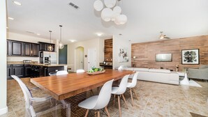 A modern kitchen with dark cabinets, a wooden island, and a dining area with clear chairs. - Paradise Palms Resort by Global Resort Homes (Kissimmee)