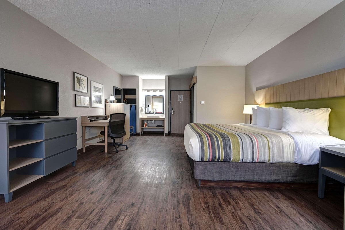 A hotel room with a bed, desk, chair, TV, and storage unit.