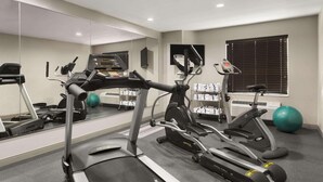 Une salle de sport équipée de tapis de course, de vélos elliptiques et de ballons d’exercice.