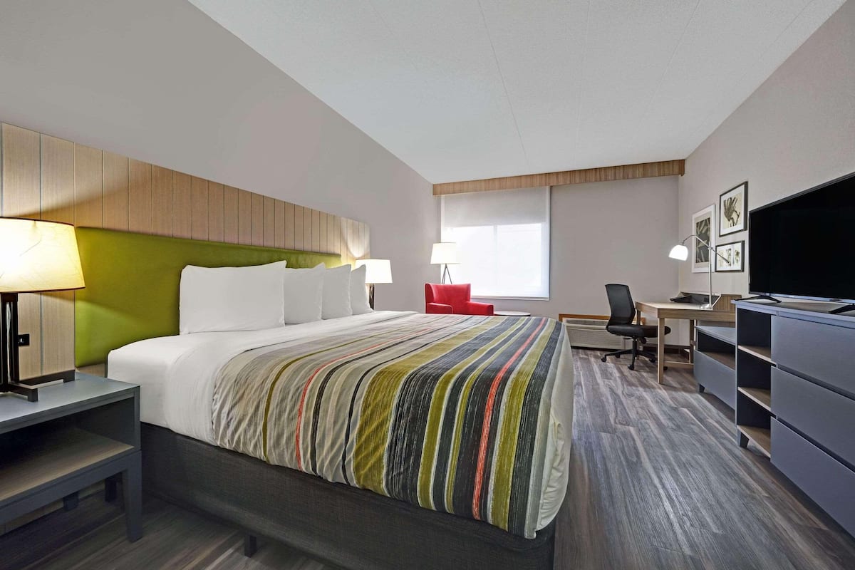 A hotel room with a bed, desk, chair, TV, and a window.