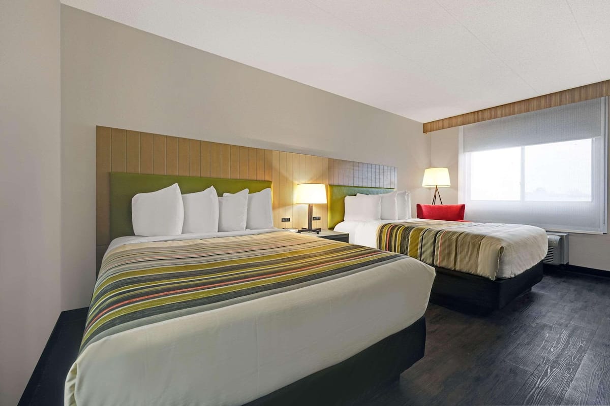 A hotel room with two beds, a wooden headboard, a large window, and a red chair.