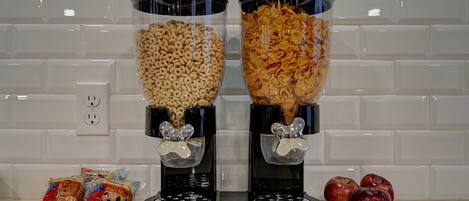 Two cereal dispensers with a white tiled backsplash and a power outlet in the background.