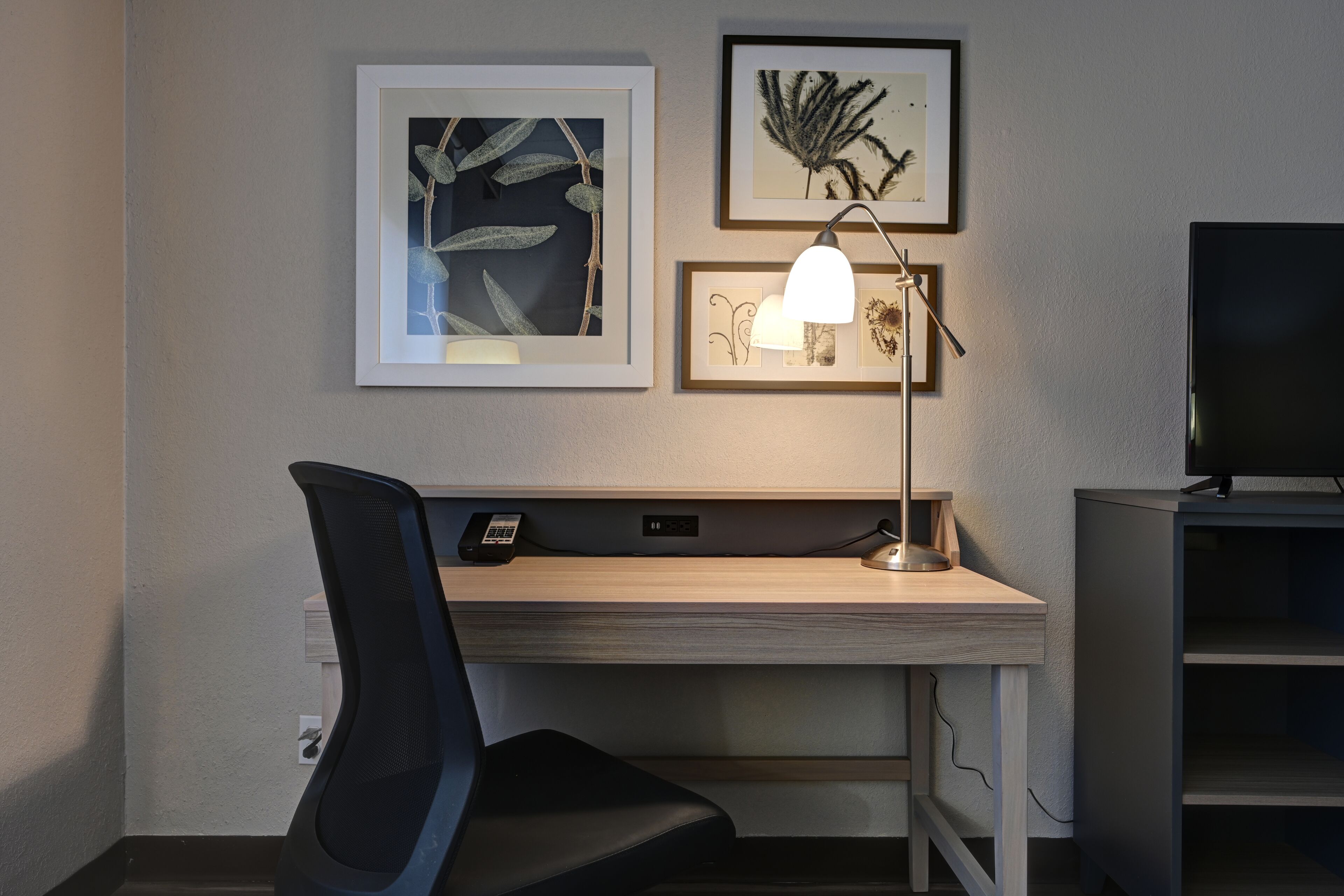 A modern hotel room with a desk, chair, and a flat-screen TV.