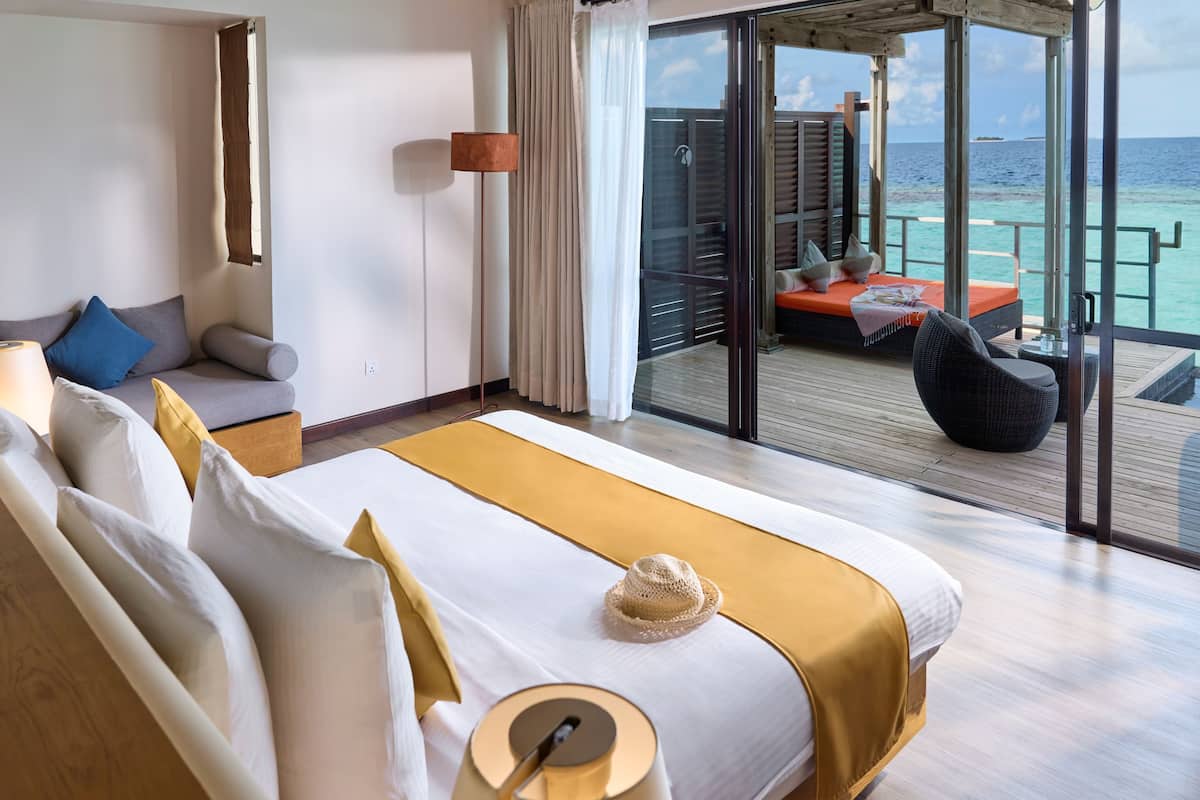 Une chambre d’hôtel avec un grand lit, un canapé, un balcon donnant sur l’océan et une terrasse en bois.