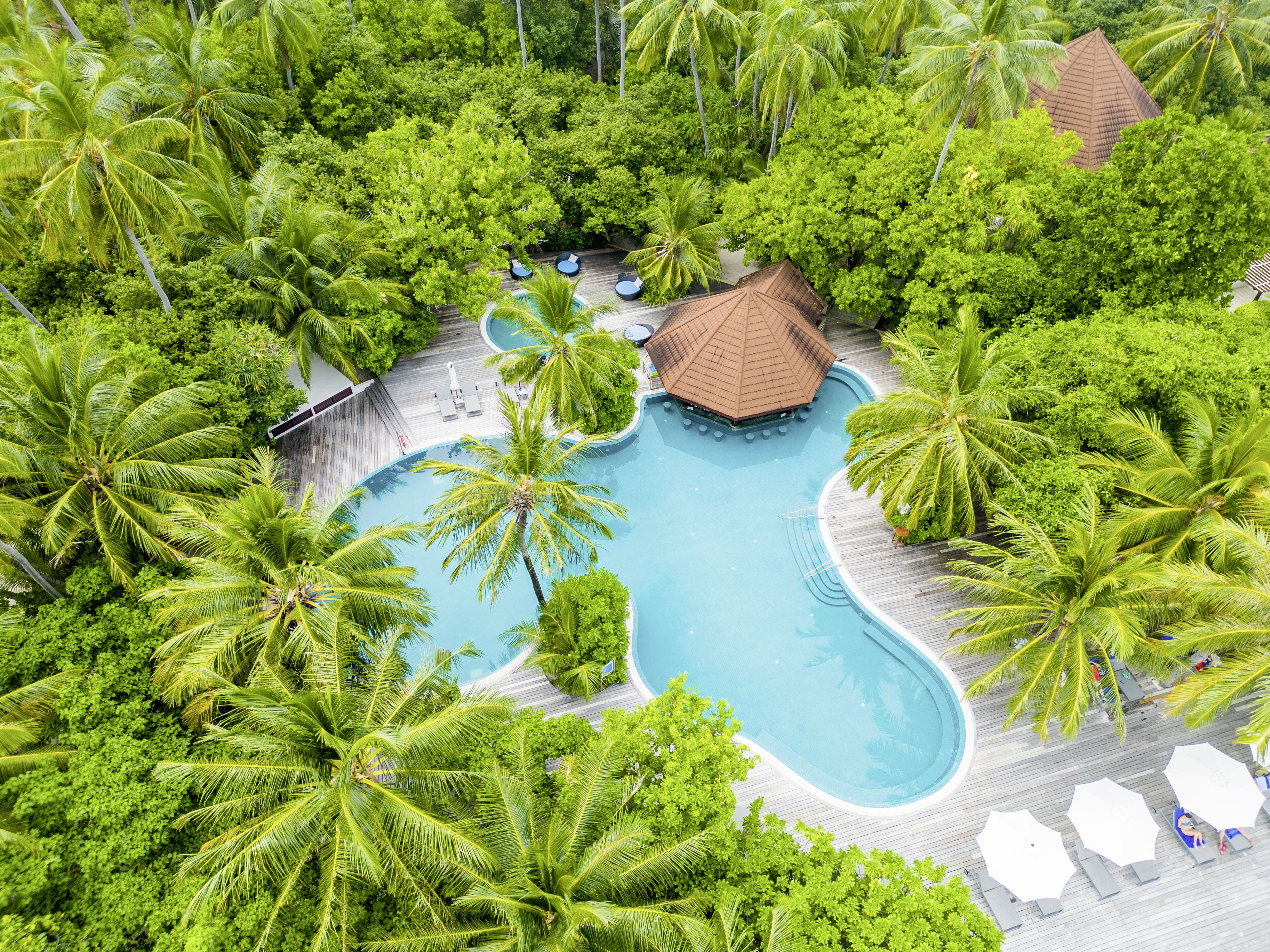 Vista aérea de um resort com uma piscina central rodeada por vegetação exuberante e palmeiras.