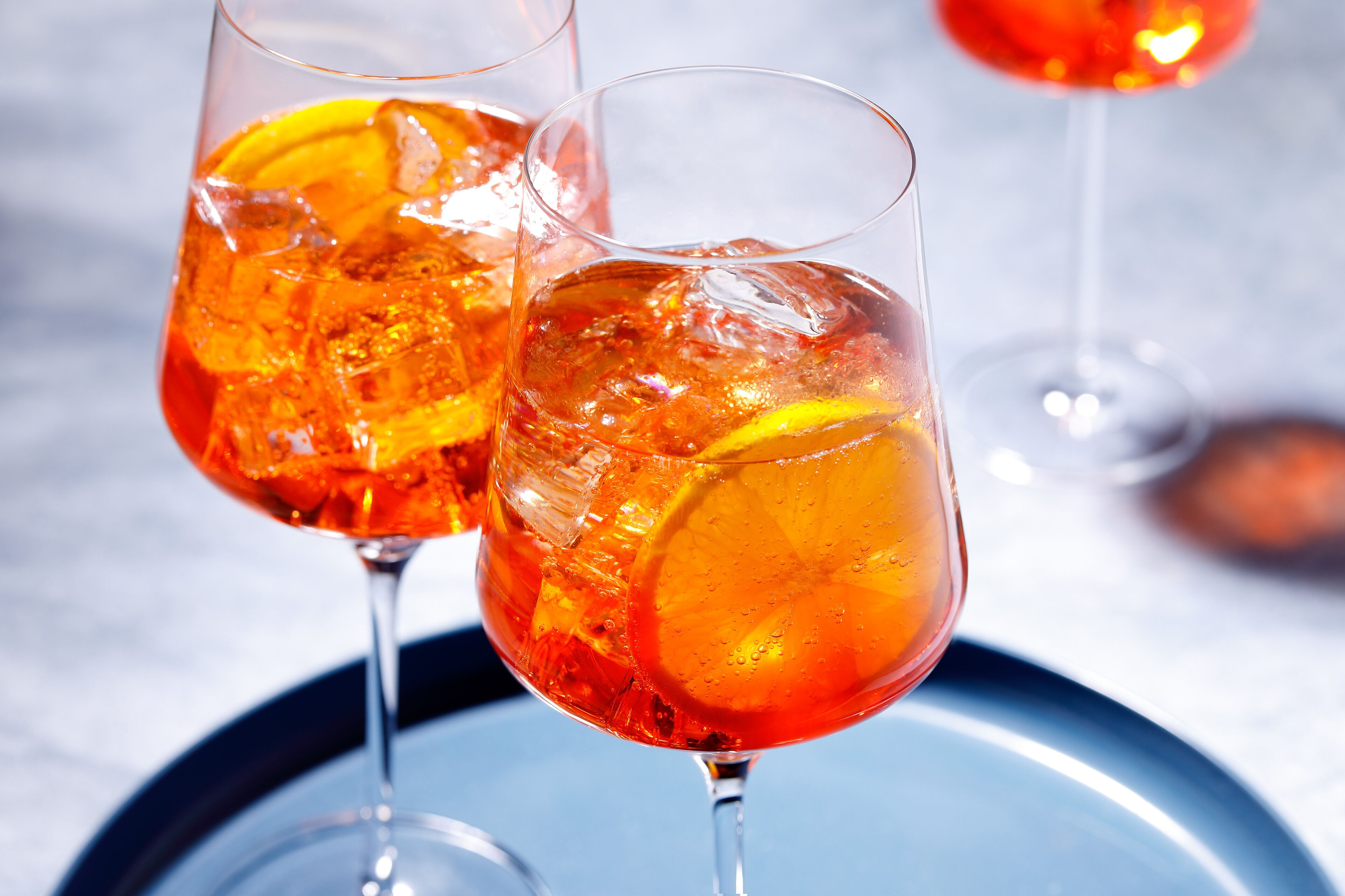 Deux verres contenant une boisson rouge, avec des glaçons et des tranches d’orange, posés sur une surface réfléchissante.