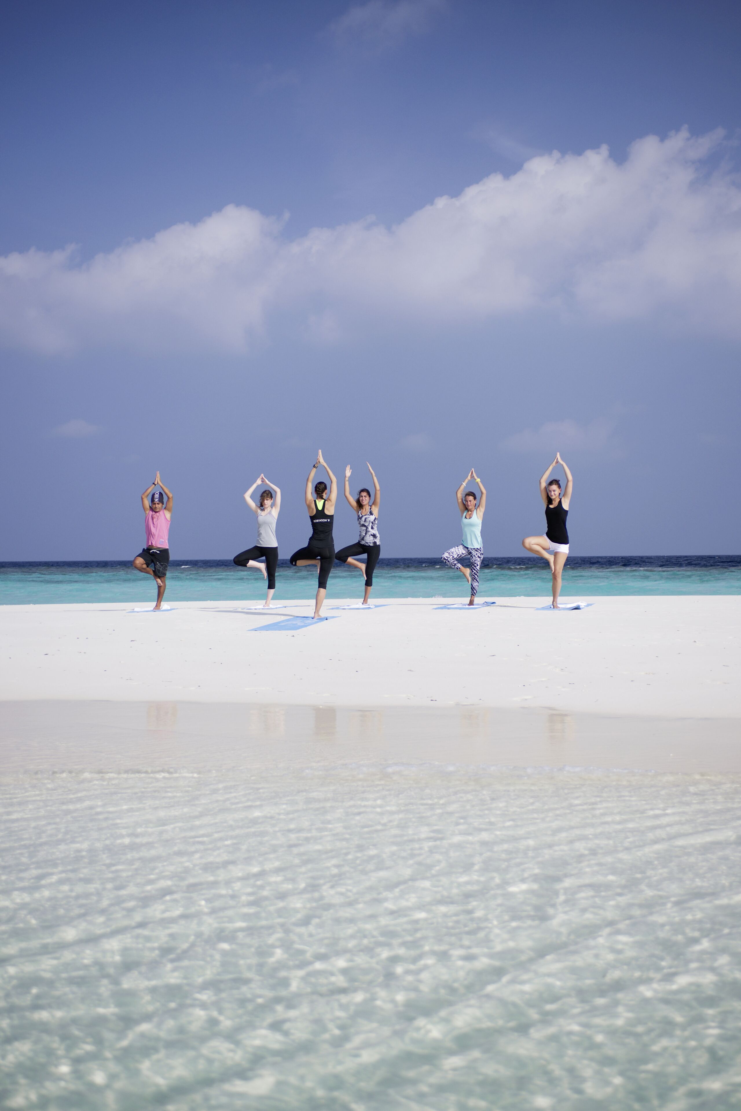 A group of people performing yoga on a beach with a clear sky and ocean in the background.