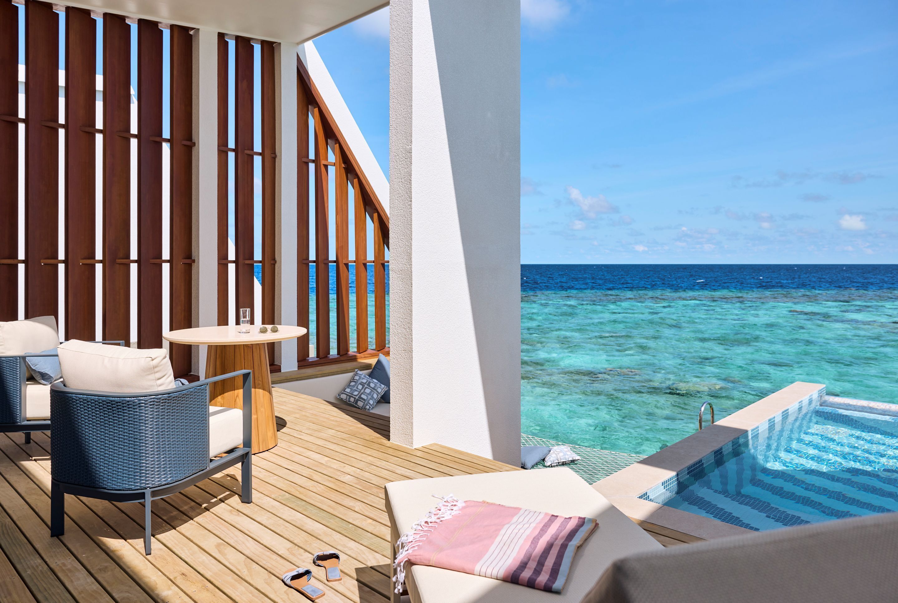 A wooden deck with a pool, lounge chairs, and a table with a glass.