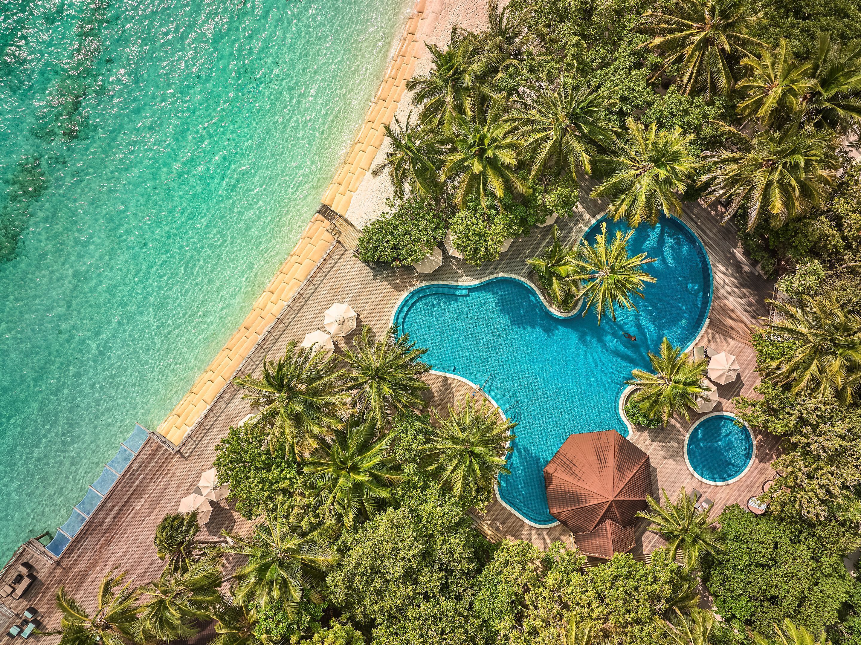 An aerial view of a resort with a large pool surrounded by palm trees and a beach.