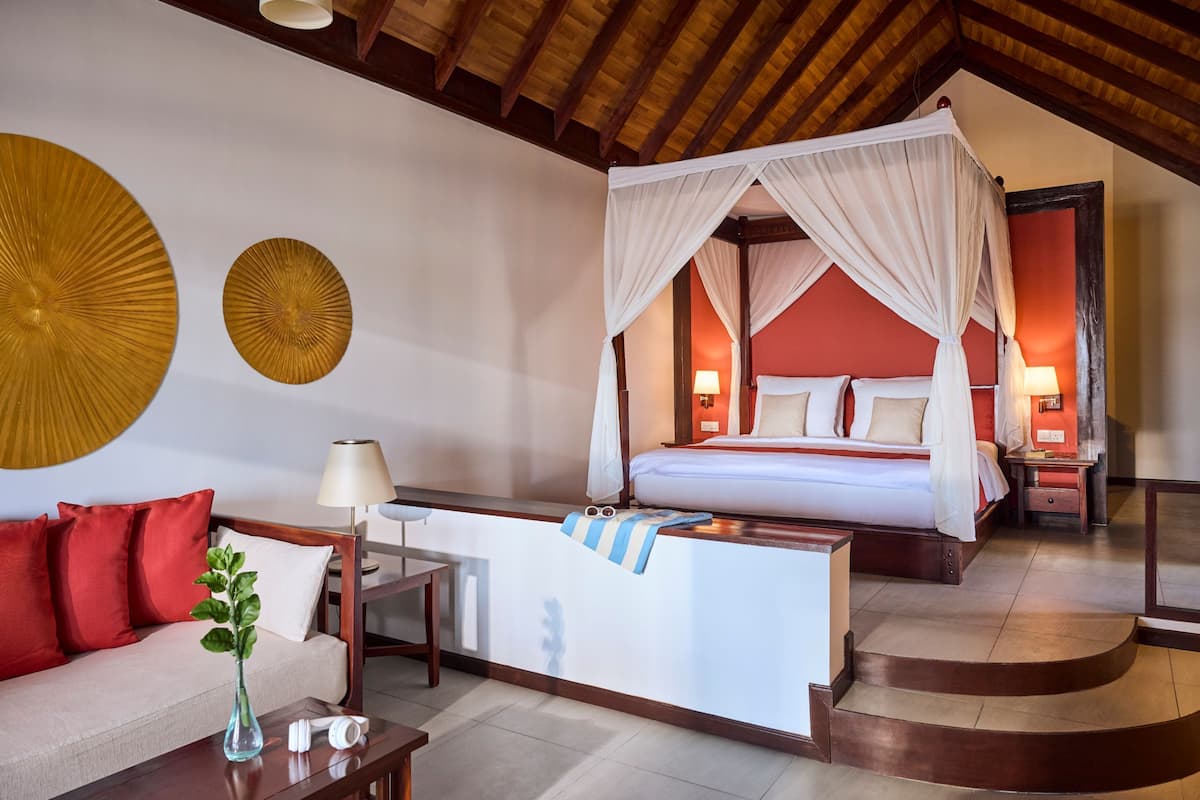 Une chambre d’hôtel dotée d’un lit à baldaquin, d’un coin salon avec un canapé et une table basse, et d’un grand élément décoratif mural.