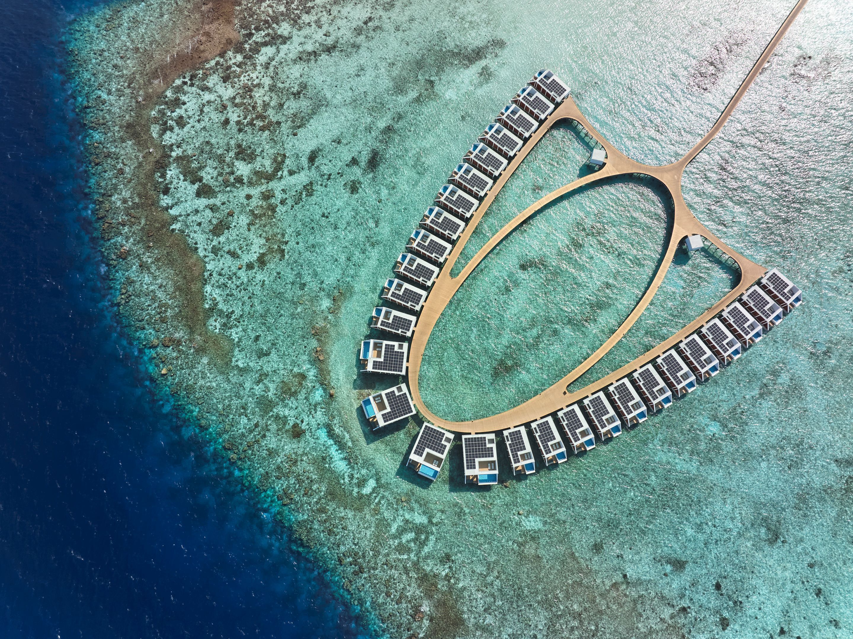 An aerial view of a resort with a crescent-shaped layout, featuring a series of connected buildings with a central lagoon.