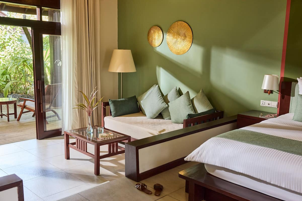 Une chambre d’hôtel avec un lit, un canapé, une table et une lampe. La fenêtre donne sur un paysage verdoyant.