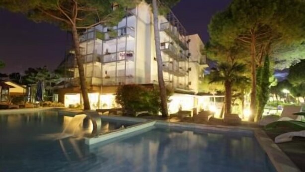A hotel with a swimming pool, outdoor seating, and a well-lit building at night. - Hotel Martini (Lignano Sabbiadoro)