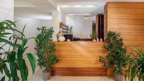 A modern reception area with a wooden reception desk, potted plants, and a seating area with a sofa and decorative items. - Hotel Martini (Lignano Sabbiadoro)