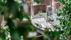 An outdoor seating area with wicker furniture and a table set for two, featuring glasses of water and a small bowl. - Hotel Martini (Lignano Sabbiadoro)