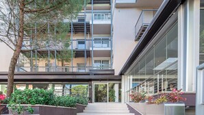 A multi-story building with a modern architectural design, featuring a central staircase leading to the entrance, surrounded by greenery and flower beds. - Hotel Martini (Lignano Sabbiadoro)