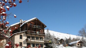 A multi-story hotel with balconies, a ski slope in the background, and snow-covered surroundings. - Le Chamois (Molines-en-Queyras)