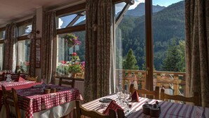 A dining area with tables set for two, large windows with curtains, and a view of a mountainous landscape. - Le Chamois (Molines-en-Queyras)