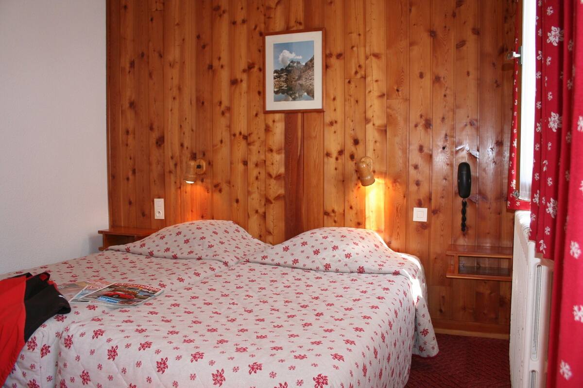 A wooden-paneled room with a bed, a framed picture on the wall, and a red curtain.