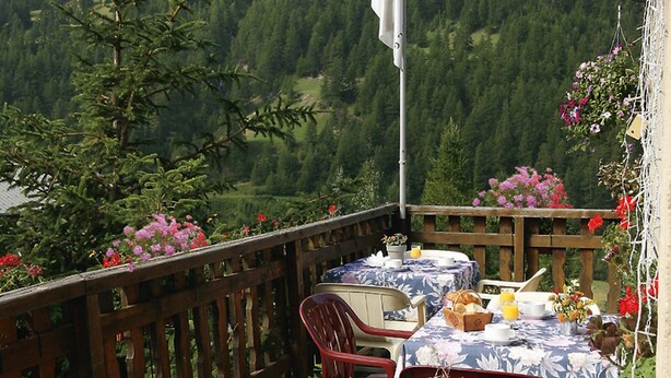 A table set for breakfast with a mountain view, a flag, and flowers. - Le Chamois (Molines-en-Queyras)