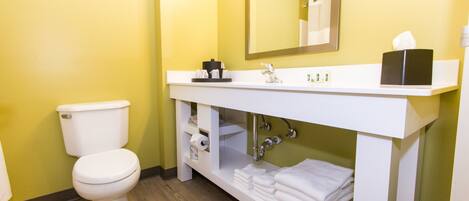 Un baño con un inodoro blanco, un lavabo con un espejo encima y una repisa con toallas.