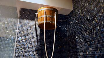 Une baignoire, un seau en bois et un tuyau d’arrosage, le tout placé devant un mur carrelé orné d’un motif en mosaïque.