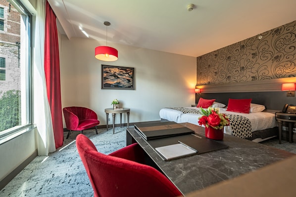 A hotel room with a bed, a desk, a chair, a small table, and a red lamp. - Van der Valk Sélys Liège Hotel & Spa (Liege)