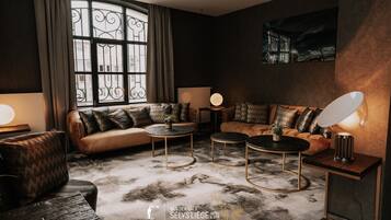 Un salon moderne avec un canapé en cuir, des tables basses rondes et une grande fenêtre agrémentée de rideaux.