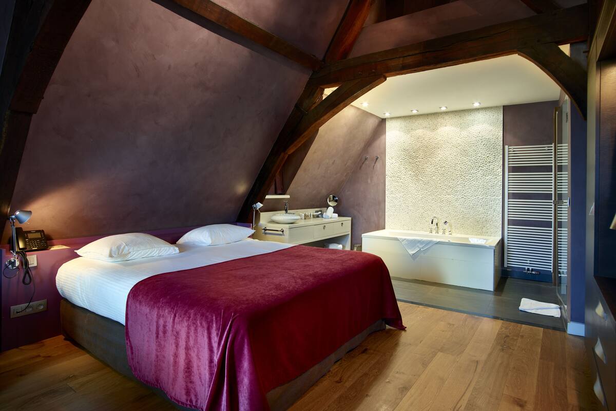 Un dormitorio con cama, mesita de noche, escritorio y baño con bañera.