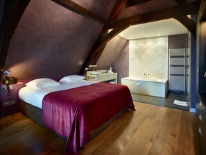 A bedroom with a bed, a nightstand, a desk, and a bathroom with a bathtub.