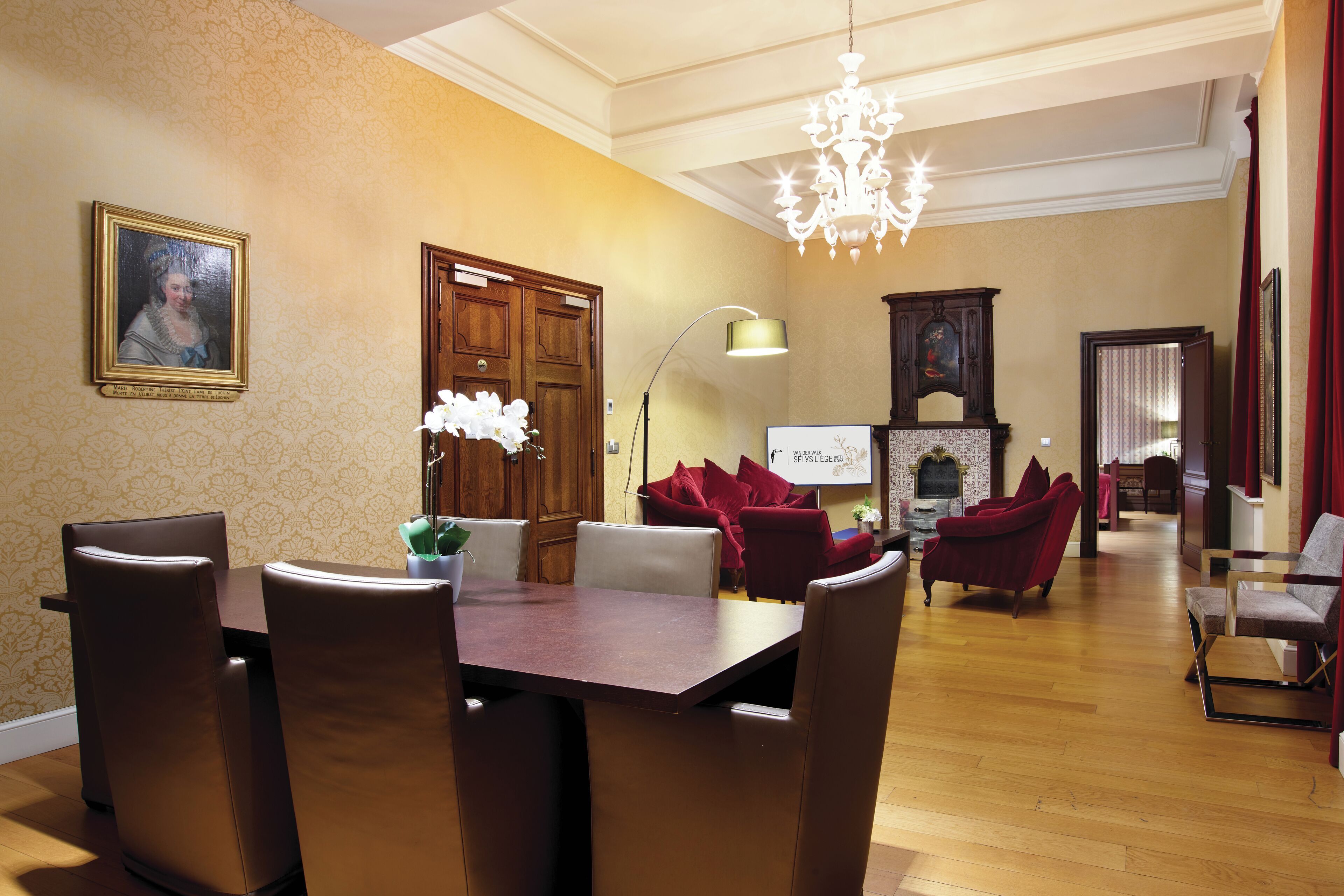 Un comedor con mesa y sillas de madera, una lámpara de araña y un sofá rojo al fondo.