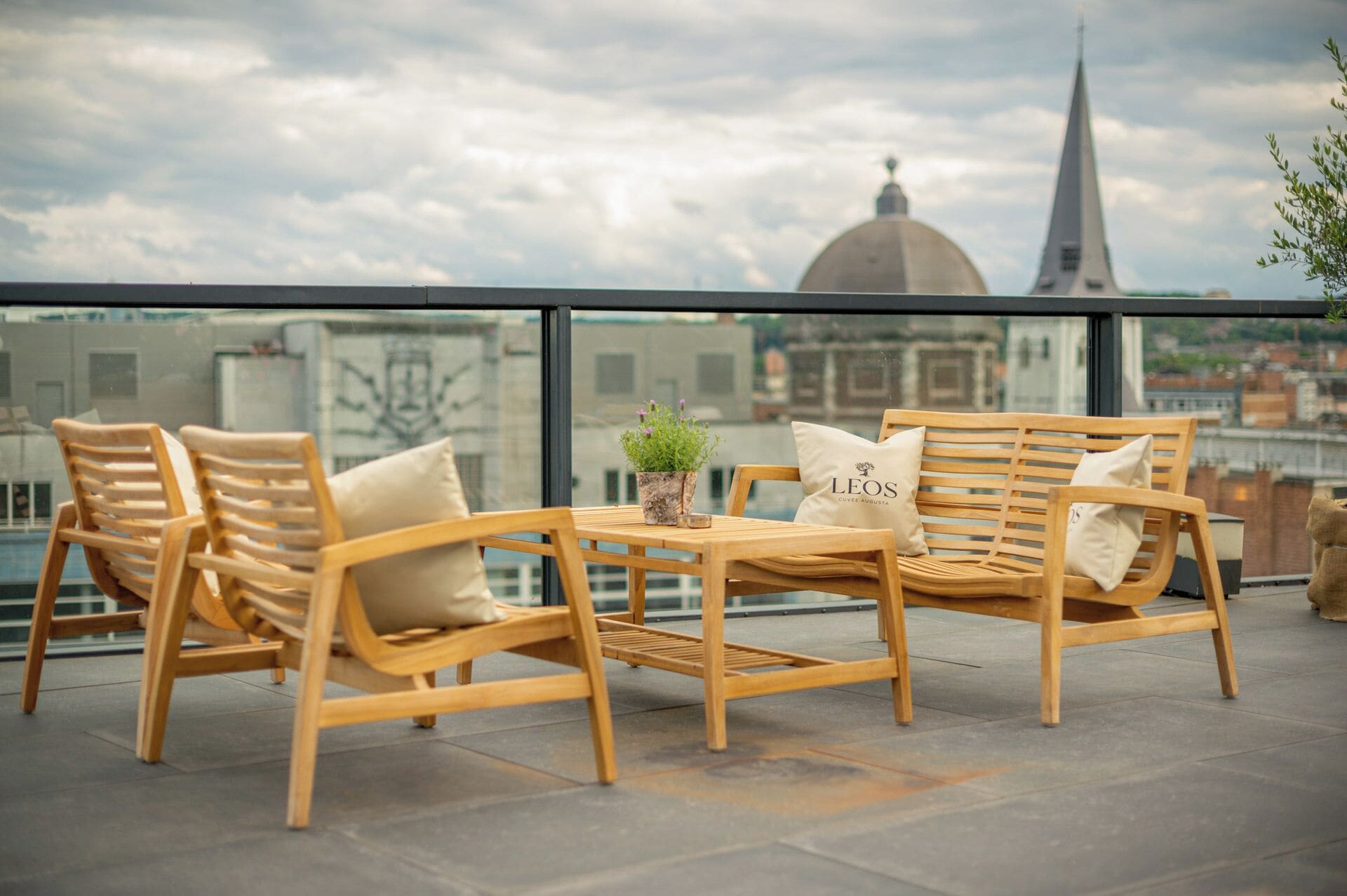 A wooden bench and chairs on a terrace with a city view, including a dome and a spire.