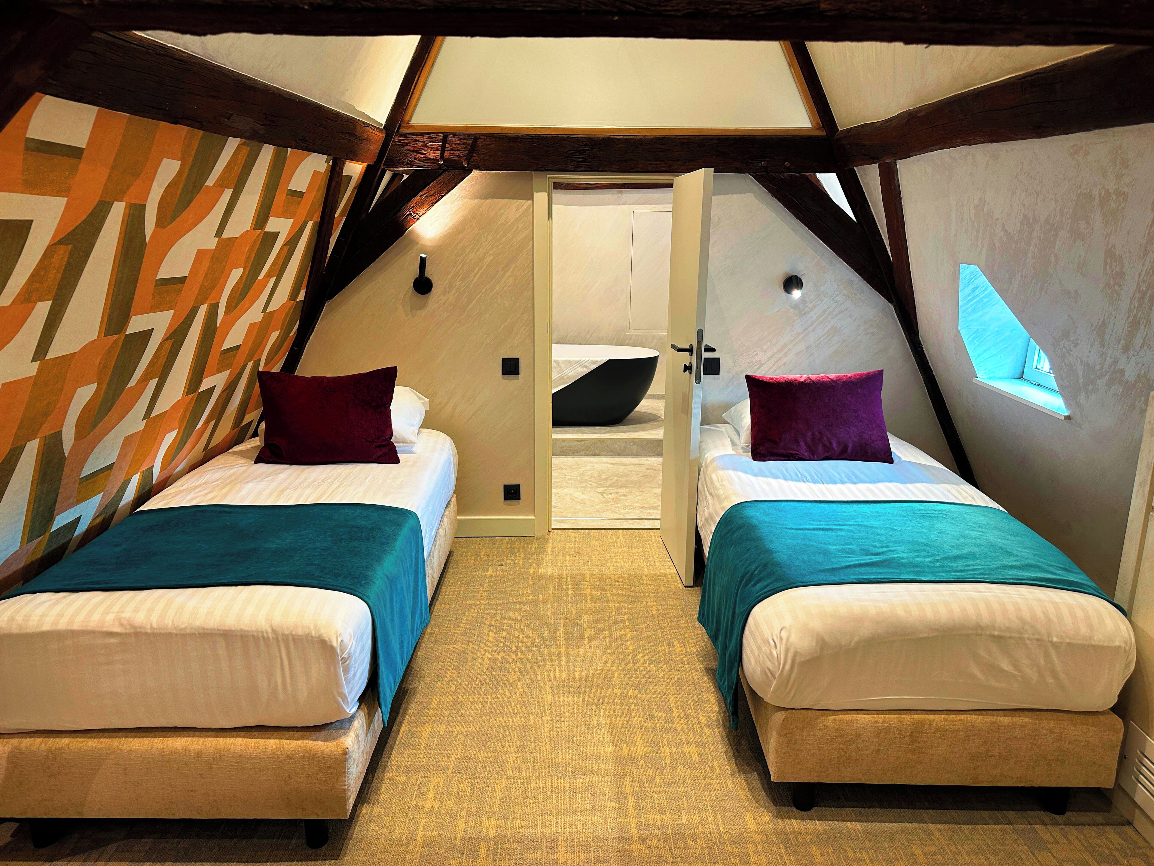 A cozy attic bedroom with two beds, a skylight, and a modern geometric wall design.