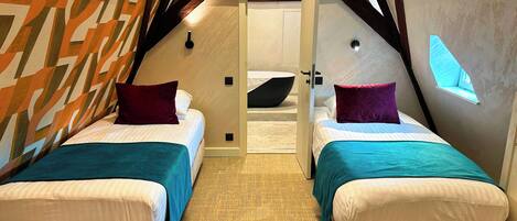 A cozy attic bedroom with two beds, a skylight, and a modern geometric wall design.
