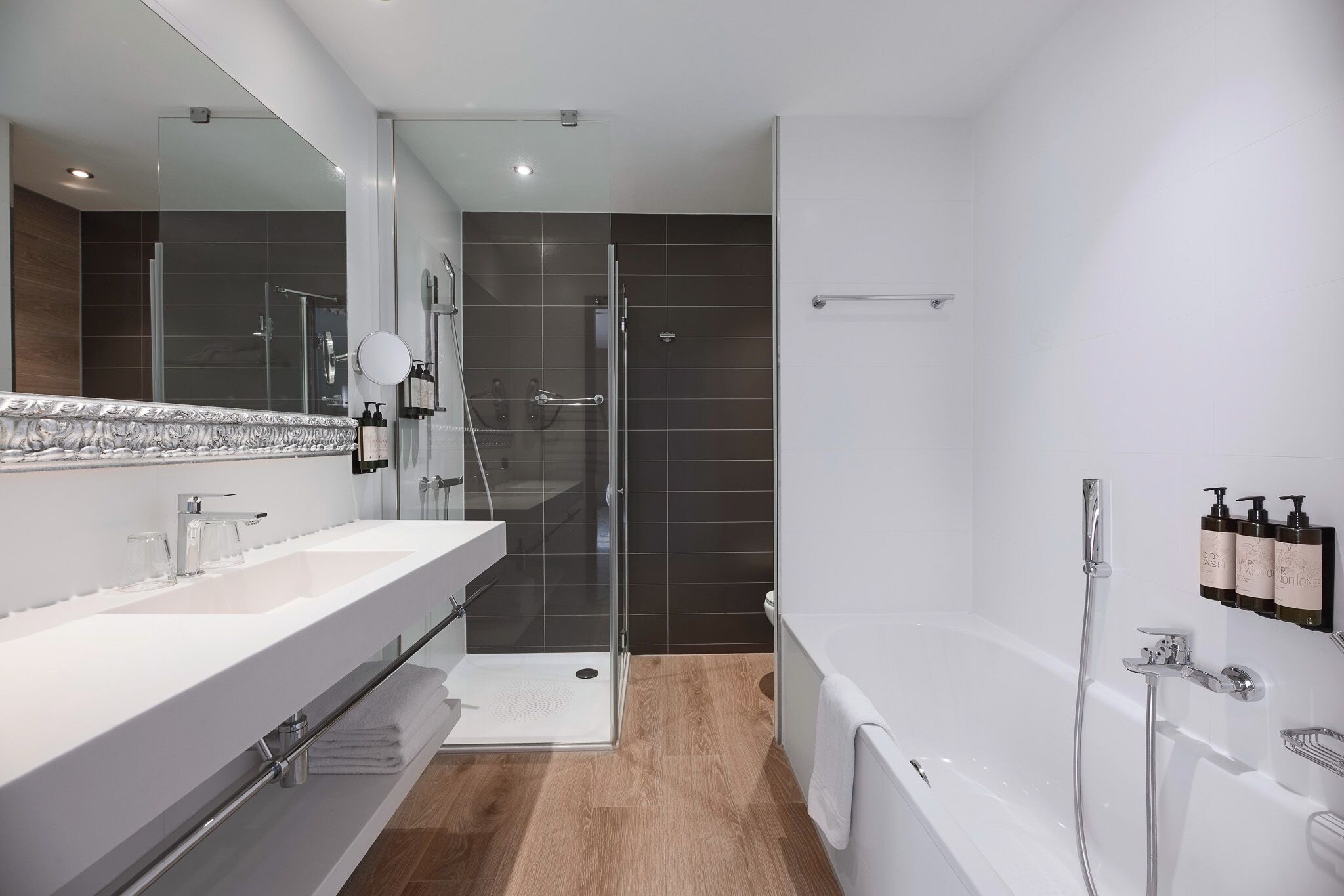 Een moderne badkamer met een douchecabine van glas, een wit bad en een grote spiegel.