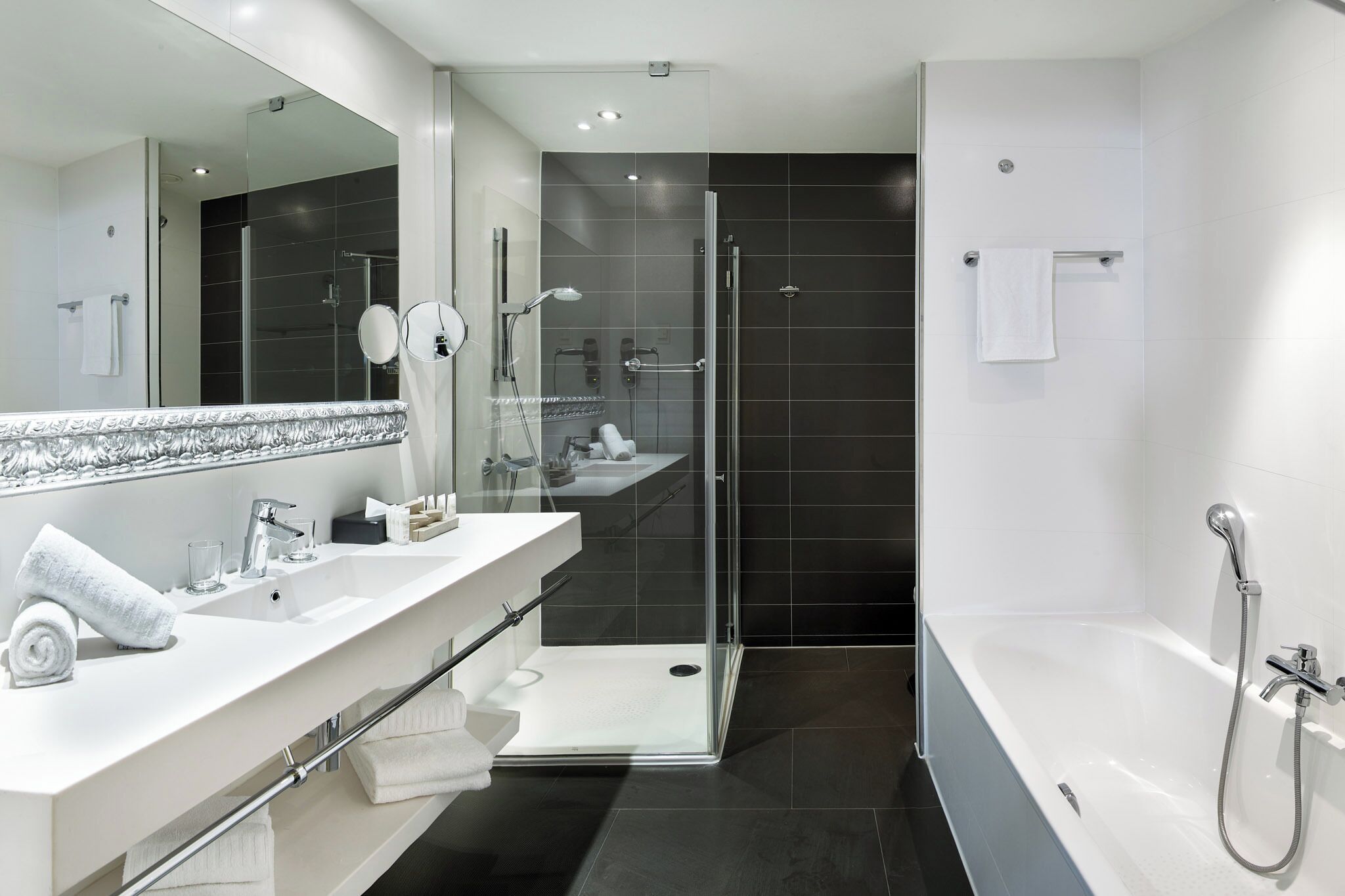 Un baño moderno con ducha de vidrio, una bañera grande y un tocador con espejo y perchero.