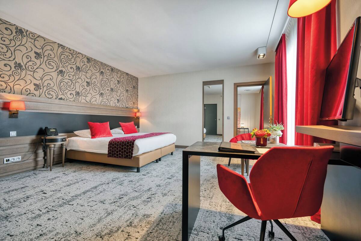 Una habitación de hotel con cama, mesita de noche, lámpara y un escritorio con silla.