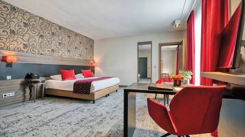 A hotel room with a bed, bedside table, lamp, and a desk with a chair.