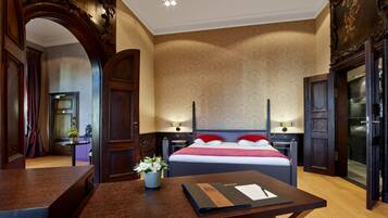 A hotel room with a large bed, a desk with a laptop, a vase of flowers, and a mirror.