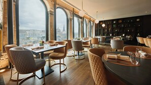 Een modern restaurant met hoge boogvensters, houten vloeren en verschillende zithoeken.