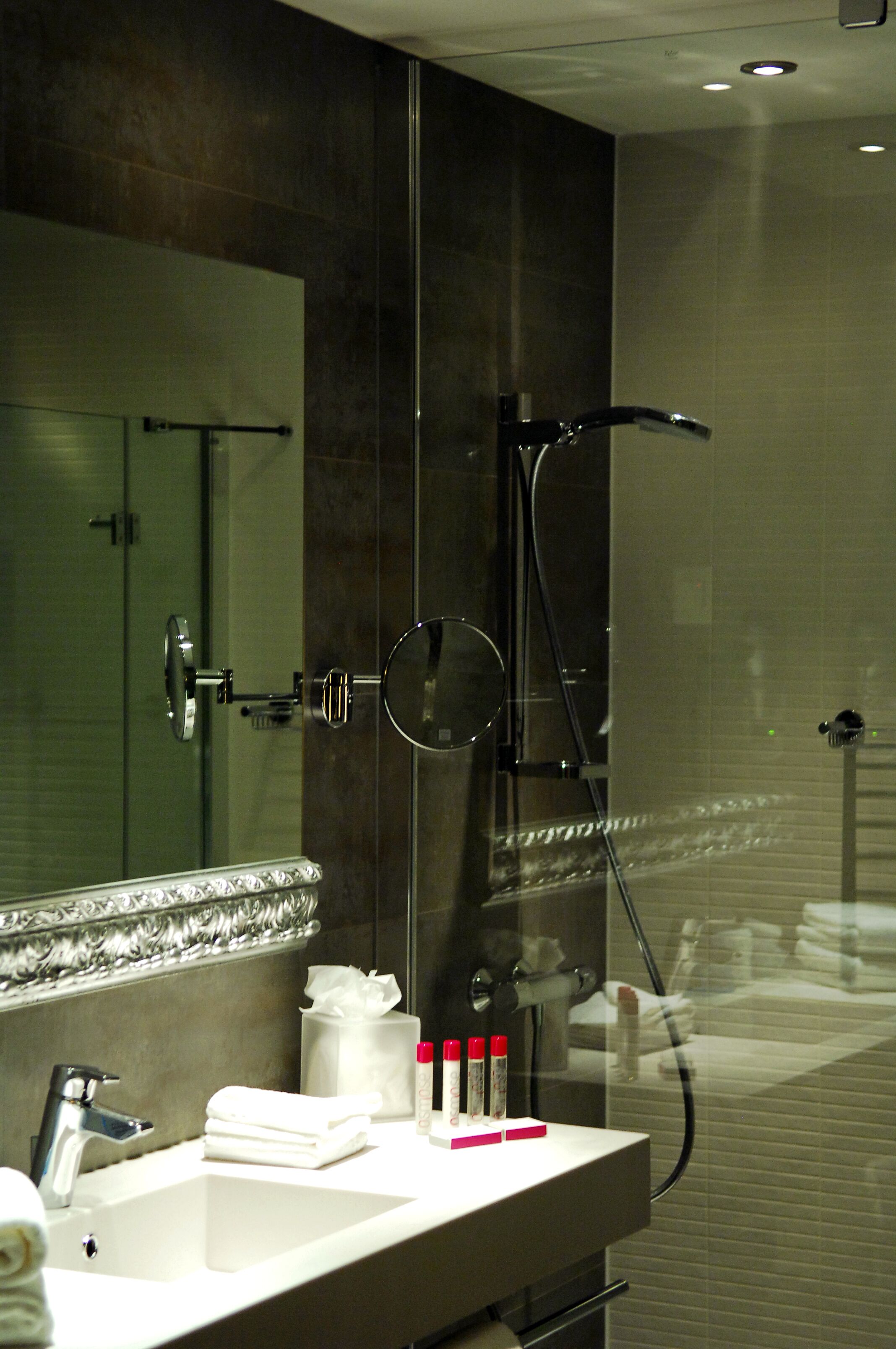 A modern bathroom with a glass-enclosed shower, a large mirror, and a white sink with toiletries.